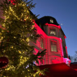 In der Bildmitte sieht man einen Anschnitt des rot angestrahlten Schloss Türnich. Ein Teil des Schlosses wird durch einen geschmückten Weihnachtsbaum am linken Bildrand verdeckt.