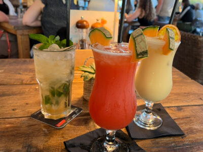 Drei bunte Cocktails stehen auf einem Holztisch.
