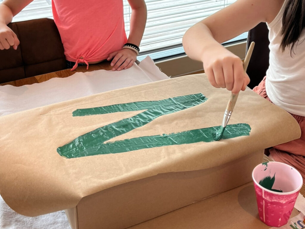 Vorbereitungen: Mit einem dicken Pinsel wird ein blaugrünes M auf Pappe gemalt.