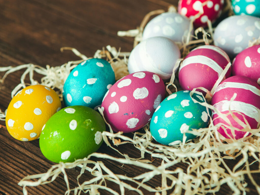 Bunt bemalte Ostereier und etwas Dekostroh auf einer dunklen Holzplatte.